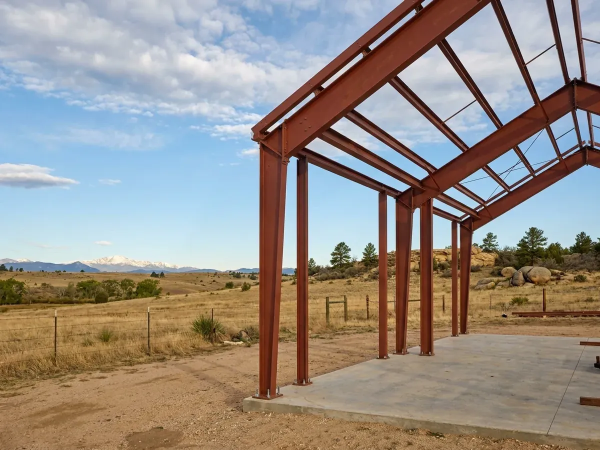 A red oxide primed structural steel frame partly erected on a concrete slab, showing bolted knee joints and anchor bolts.